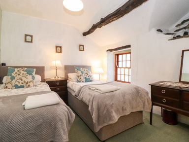 A bedroom with two single beds a nightstand with lamps and a wooden dresser with a mirror at Castle Lodge in Borrowdale