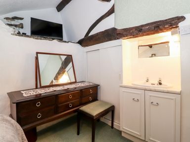 A room with a wooden dresser with a mirror and a stool beside a white sink cabinet with exposed wooden ceiling beams at Castle Lodge in Borrowdale