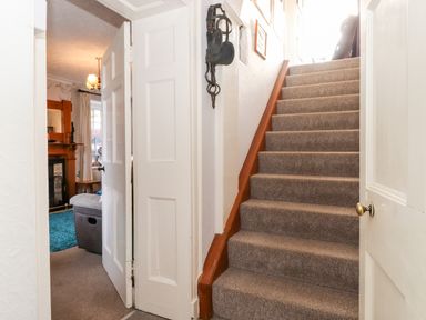 A carpeted staircase next to an open door leading to a living room with a fireplace at Castle Lodge in Borrowdale