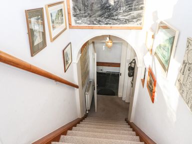 A staircase with carpeted steps and wooden handrail leading down to a doorway with framed pictures on the walls at Castle Lodge in Borrowdale