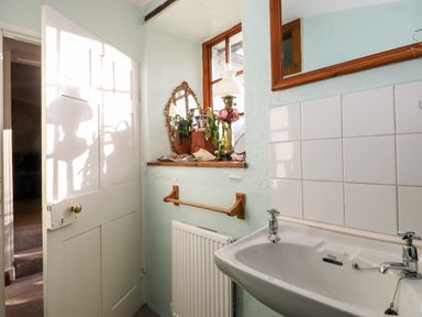A small bathroom with a white sink a wooden framed mirror a window shelf with a lamp a mirror and plants at Castle Lodge in Borrowdale
