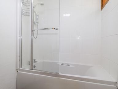 A bathroom with a bathtub shower enclosure and white tiled walls at Castle Lodge in Borrowdale
