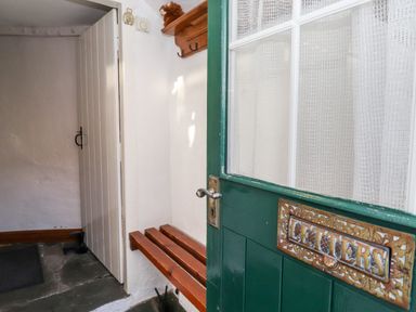 An entrance area with a green door that has a letters slot and a wooden bench mounted on a white wall at Castle Lodge in Borrowdale