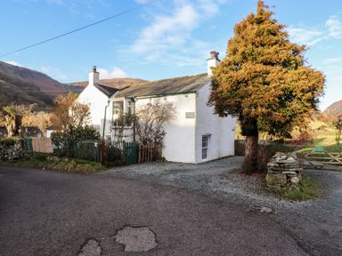 A white house with chimneys and a tree in front by a gravel driveway at Castle Lodge in Borrowdale