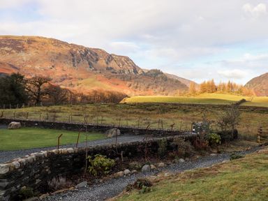 A garden with stone walls and gravel paths with hills and trees in the background at Castle Lodge in Borrowdale