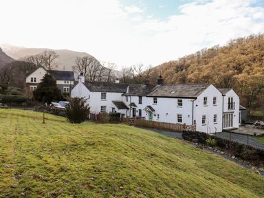 A row of white houses with slate roofs surrounded by grass and trees at Castle Lodge in Borrowdale