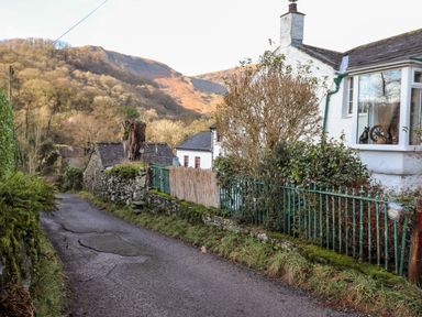 A narrow road with stone walls and houses surrounded by trees and hills at Castle Lodge in Borrowdale