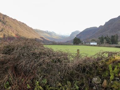 A green field with a wire fence and stone wall in front of mountains and houses at Castle Lodge in Borrowdale
