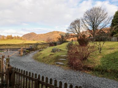 A gravel driveway with wooden gates and picket fence leading to grassy hills and trees at Castle Lodge in Borrowdale