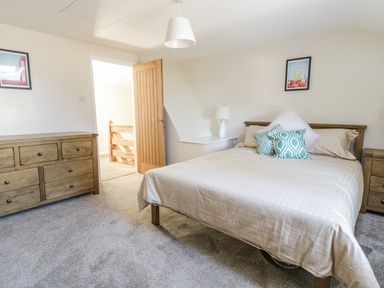 A bedroom with a bed with pillows a wooden dresser and an open door at Y Cilgwyn in Trawsfynydd