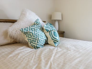 A bed with patterned pillows and a white furry cushion next to a bedside table with a lamp at Y Cilgwyn in Trawsfynydd