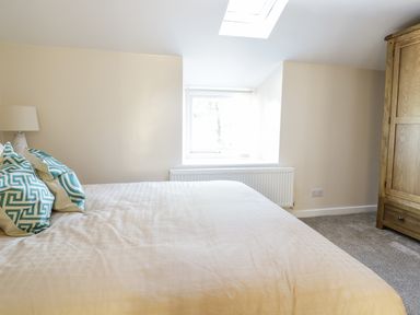 A bedroom with a bed with patterned pillows a lamp a window and a wooden wardrobe at Y Cilgwyn in Trawsfynydd