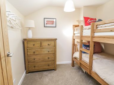 A bedroom with a wooden chest of drawers a lamp bunk beds and a framed picture of a double-decker bus at Y Cilgwyn in Trawsfynydd