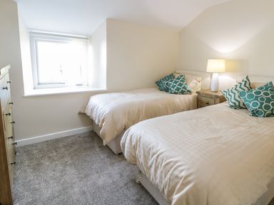 A bedroom with two single beds with beige bedding a wooden nightstand with a lamp and a wooden dresser near a window at Y Cilgwyn in Trawsfynydd