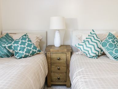 A bedroom with two beds separated by a wooden nightstand with a white lamp on top at Y Cilgwyn in Trawsfynydd