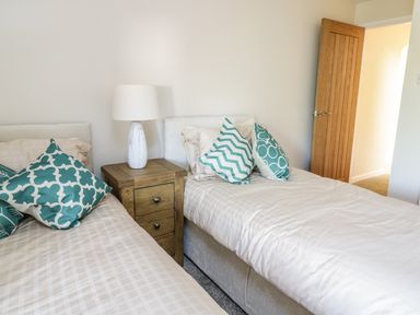 A bedroom with two single beds separated by a wooden nightstand with a lamp and decorative pillows at Y Cilgwyn in Trawsfynydd