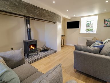 A living room with a wood burning stove between two sofas a wall mounted television a window and wooden flooring at Y Cilgwyn in Trawsfynydd
