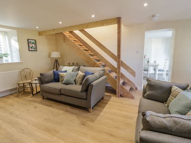 A living room with two grey sofas under wooden stairs and a dining room visible through a doorway at Y Cilgwyn in Trawsfynydd