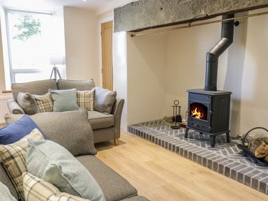 A living room with sofas and a wood burning stove on a brick hearth at Y Cilgwyn in Trawsfynydd