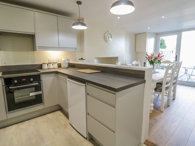 A kitchen with white cabinets a countertop oven and a dining table with flowers at Y Cilgwyn in Trawsfynydd