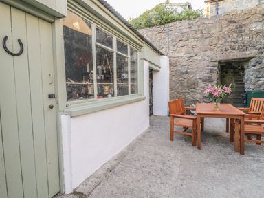 An outdoor patio area with wooden table and chairs and a vase of flowers near a stone wall and green door at Y Cilgwyn in Trawsfynydd