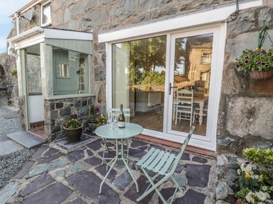A small patio with a round table and two chairs outside a stone building with sliding glass doors at Y Cilgwyn in Trawsfynydd