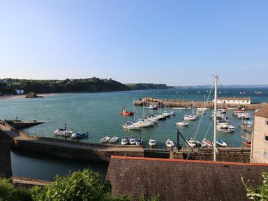 A harbor with boats docked along piers and a shoreline with buildings and hills at Pottery Cottage in Begelly near Kilgetty