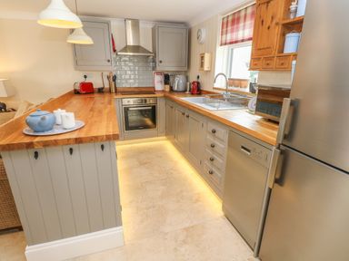 A kitchen with wooden countertops gray cabinets a sink oven dishwasher and stainless steel refrigerator at Pottery Cottage in Begelly near Kilgetty