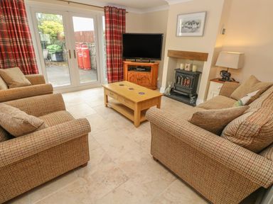 A living room with sofas a coffee table a television wood stove and glass doors at Pottery Cottage in Begelly near Kilgetty