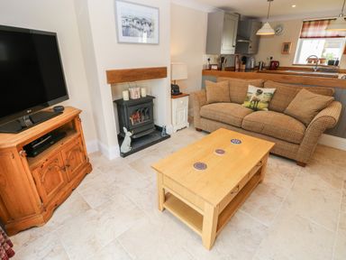 A living room with a sofa and coffee table near a fireplace and television at Pottery Cottage in Begelly near Kilgetty