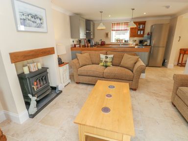 A living room with a sofa cushions and a wooden coffee table near a fireplace and an open kitchen at Pottery Cottage in Begelly near Kilgetty