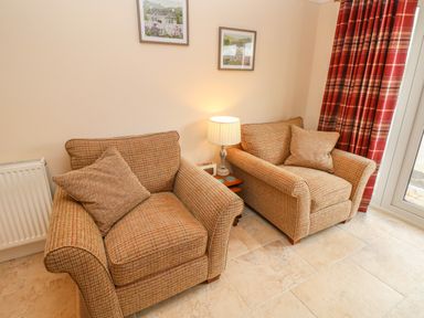 A sitting area with two armchairs a lamp on a side table and red patterned curtains at Pottery Cottage in Begelly near Kilgetty