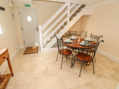 A dining area with a round table set for four under stairs with a door in the background at Pottery Cottage in Begelly near Kilgetty