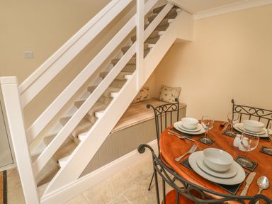 A dining table set with plates bowls and glasses next to a staircase with a cushioned bench underneath at Pottery Cottage in Begelly near Kilgetty
