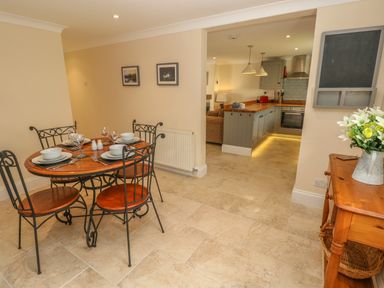 A dining area with a wooden table set for four and visible kitchen area with wooden counters at Pottery Cottage in Begelly near Kilgetty