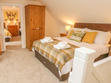 A bedroom with a double bed with pillows and folded towels a wooden wardrobe and a doorway to another bedroom at Pottery Cottage in Begelly near Kilgetty