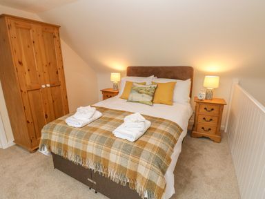 A bedroom with a double bed with pillows and folded towels a wardrobe and two bedside tables with lamps at Pottery Cottage Begelly near Kilgetty