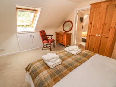 A bedroom with a bed covered with folded towels and a checkered blanket with a wooden chair a dresser with a mirror and a wooden wardrobe at Pottery Cottage in Begelly near Kilgetty