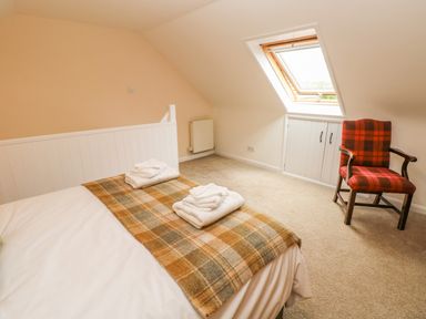 A bedroom with a bed with folded towels and a plaid blanket a red chair and a skylight window at Pottery Cottage in Begelly near Kilgetty