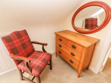 A red and brown plaid armchair next to a wooden dresser with a round red framed mirror above it at Pottery Cottage in Begelly near Kilgetty
