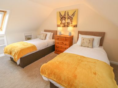 A bedroom with two single beds yellow throws and a wooden chest of drawers with lamps and a donkey painting at Pottery Cottage in Begelly near Kilgetty