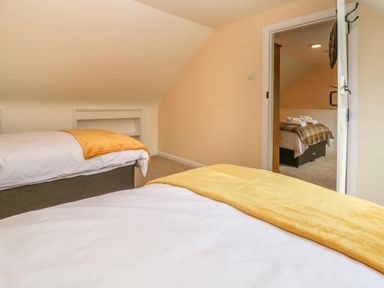 A bedroom with two beds and yellow blankets and a view into another room with a bed at Pottery Cottage in Begelly near Kilgetty