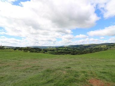 A green field with hills trees and clouds in the sky at Shepherds View in Rhayader