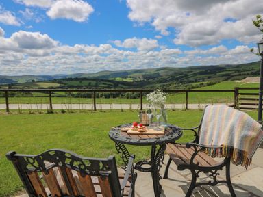 A garden with a metal and wooden table and chairs with snacks and drinks and a blanket overlooking hills and fields at Shepherd's View in Rhayader