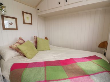 A bedroom with a bed covered in white sheets and a colorful green and pink blanket at Shepherd's View in Rhayader