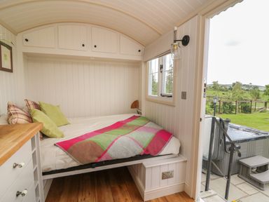 A small bedroom with a bed with cushions and a blanket next to a window and an open door leading outside at Shepherd's View in Rhayader