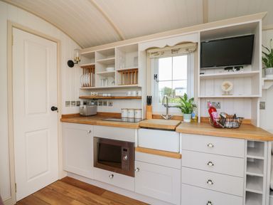 A kitchen with white cabinets wooden countertops a microwave toaster sink window and small television at Shepherd's View in Rhayader