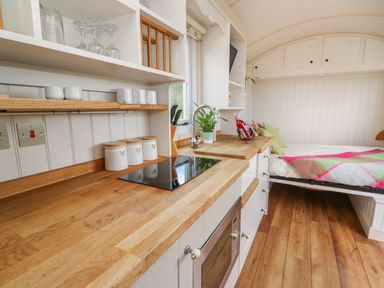 A small kitchen area with wooden countertops white cabinets a sink an electric stove and a bed with a colorful blanket at Shepherds View in Rhayader