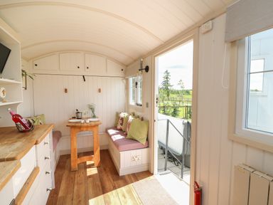 A small dining area with bench seating, table, cushions, and kitchen counter next to an open door in Shepherd's View in Rhayader