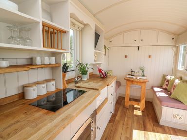 A kitchen space with wooden countertops white cabinets a small dining table and bench seating at Shepherd's View in Rhayader